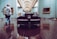 A spacious room in an art gallery features several paintings displayed on the walls. The central focus is a luxurious, dark leather circular bench on a shiny wooden floor. People are casually observing the artworks, creating a relaxed atmosphere.