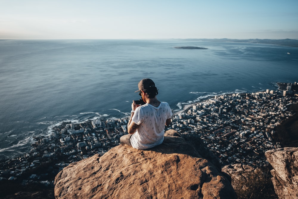 man sitting on brown rock near water during daytime photo