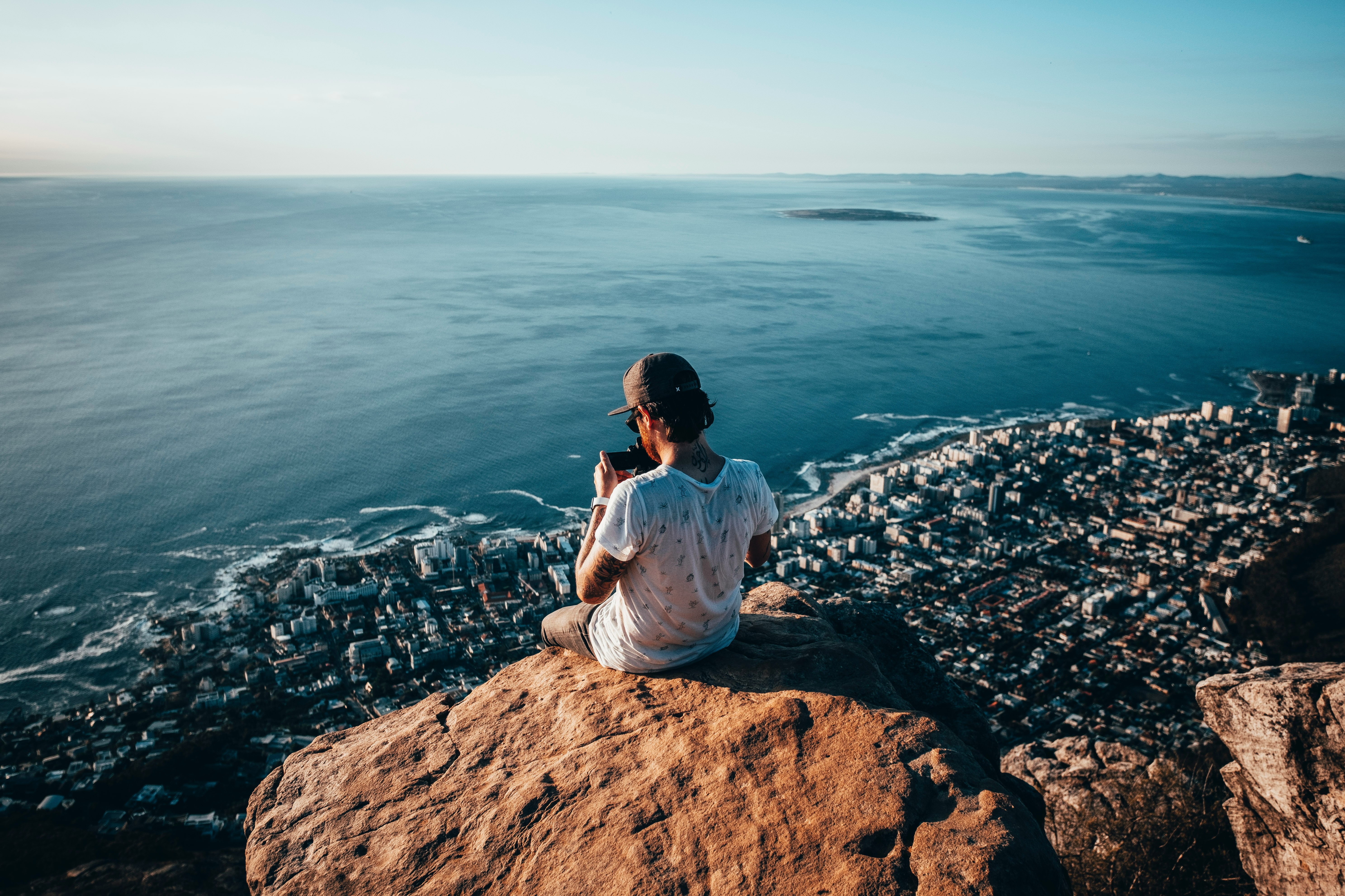 man sitting on brown rock near water during daytime photo