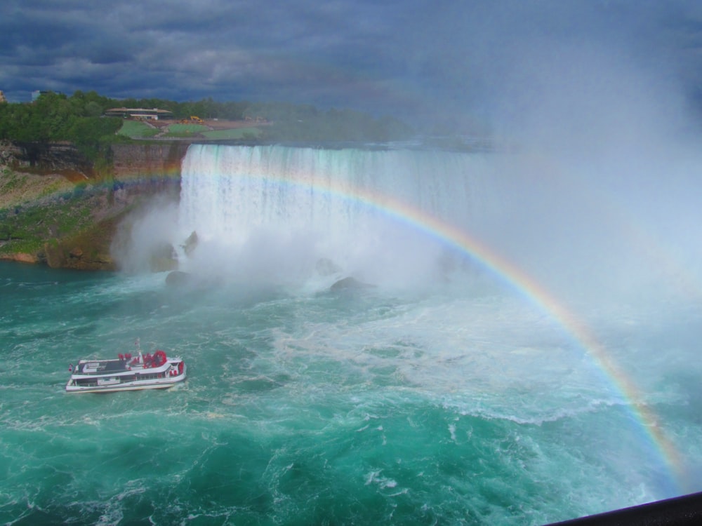 white and black fishing boat in blue ocean water under rainbow during daytime