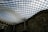 A large, curved glass roof structure covers a historic building, creating a modern architectural feature. The grid pattern of the glass panels allows natural light to filter through, casting a geometric shadow on the stone facade below.