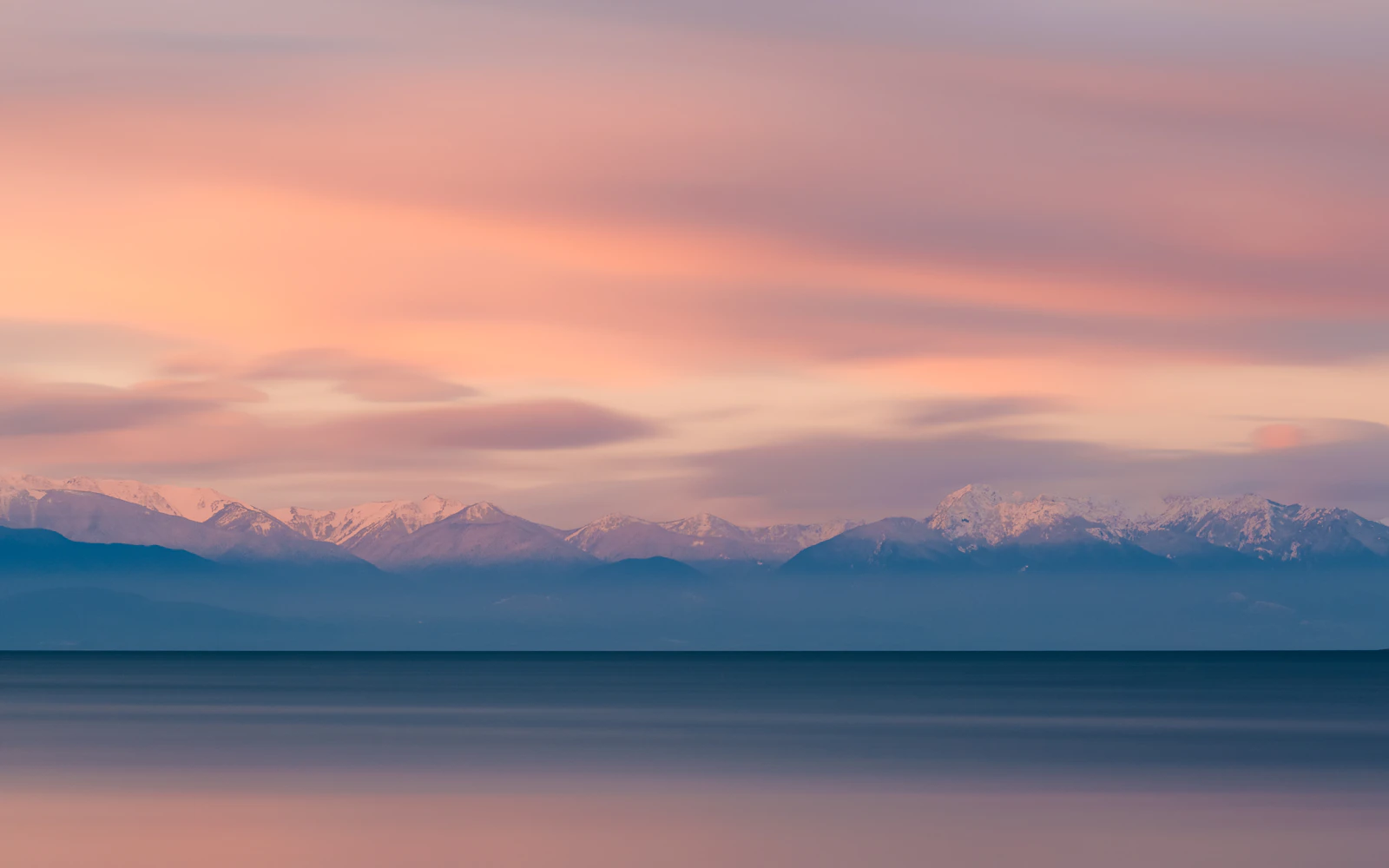 Snow-dusted Olympic mountains under a pastel pink sky across smooth open water at dusk