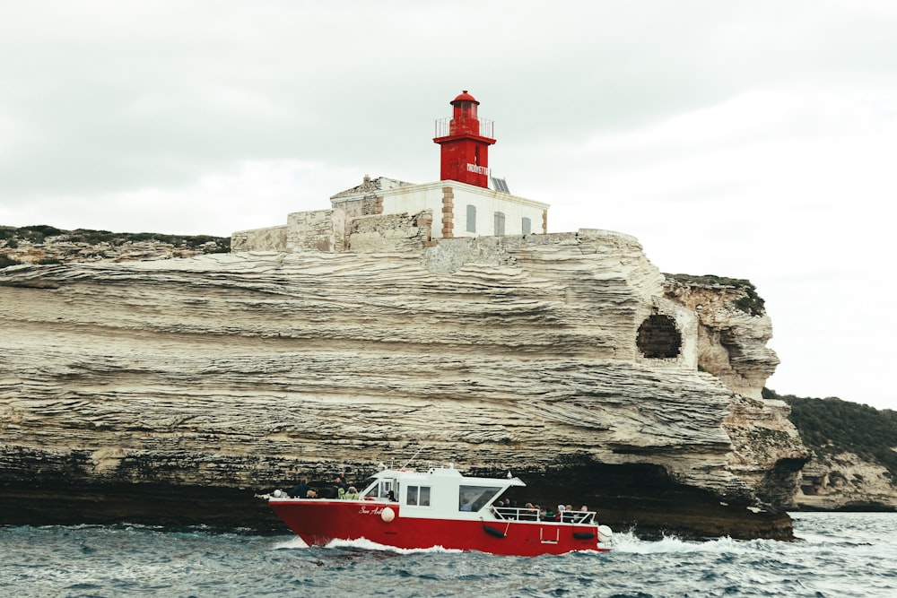 昼間の灰色の岩層近くの水域に浮かぶ赤と白のボート