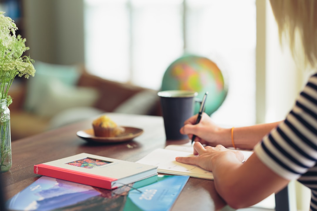 shallow focus photography of person in white and black striped top writing on white paper