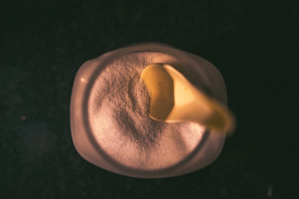 Poudre blanche et cuillère jaune à l’intérieur d’un bocal en verre transparent