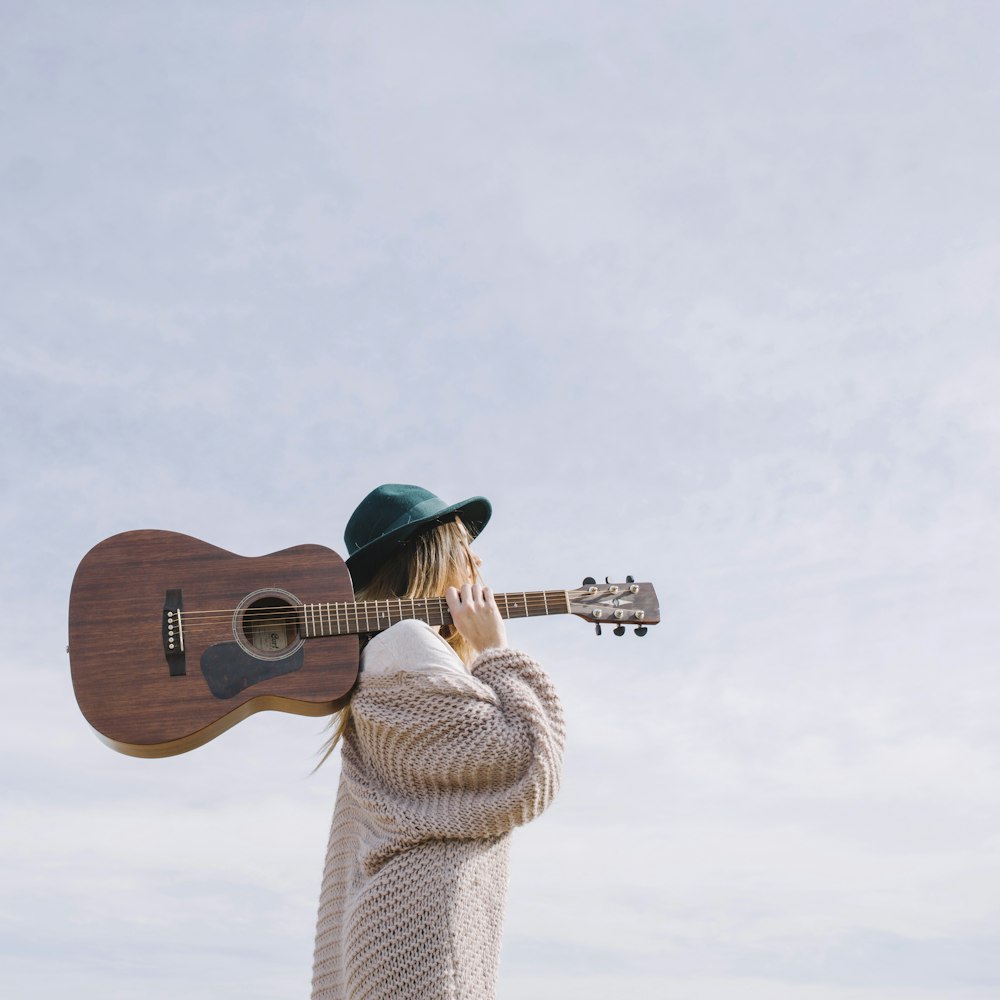 woman carrying brown acoustic guitar