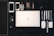 A neatly arranged collection of everyday items is displayed on a dark surface. At the center is an open laptop, surrounded by various objects such as two smartphones, a set of earphones, multiple pens, a mouse, sunglasses, a watch, a wallet, a small notebook, a ruler, a packet of mints, and a metal pen. The arrangement suggests organization and preparedness.