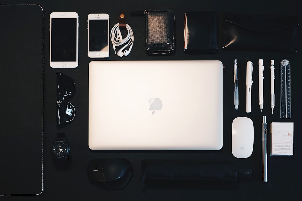 MacBook argenté entre Magic Mouse, crayon, lunettes de soleil et iPhone