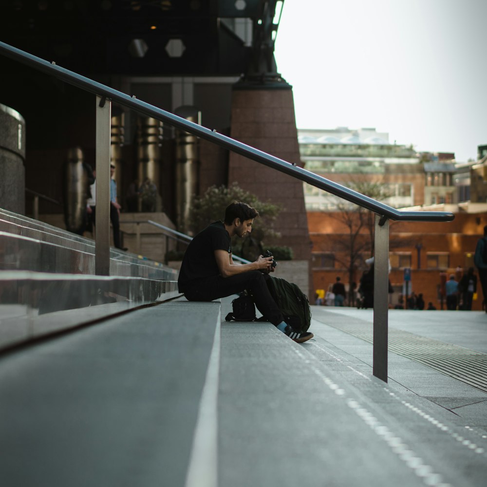 man sitting on concrete stair near road during daytime