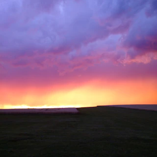 A vibrant sunset over Zimbabwean farmland, with golden hues blending into a purple sky.