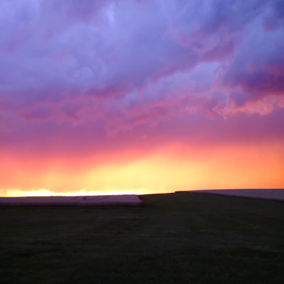 A vibrant sunset over Zimbabwean farmland, with golden hues blending into a purple sky.
