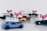 Several miniature toy cars are arranged with blurred Uber and Lyft logos. The cars are differently colored, including shades of blue, green, and gold, and are set against a plain background.