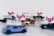 Several miniature toy cars are arranged with blurred Uber and Lyft logos. The cars are differently colored, including shades of blue, green, and gold, and are set against a plain background.