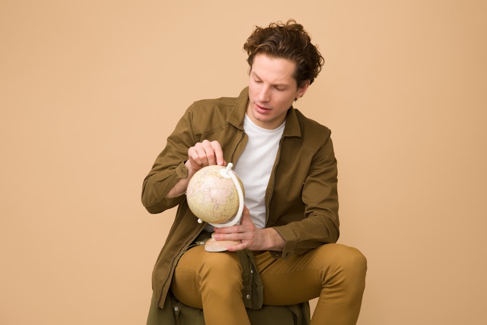 homme tenant un globe pendant qu’il est assis