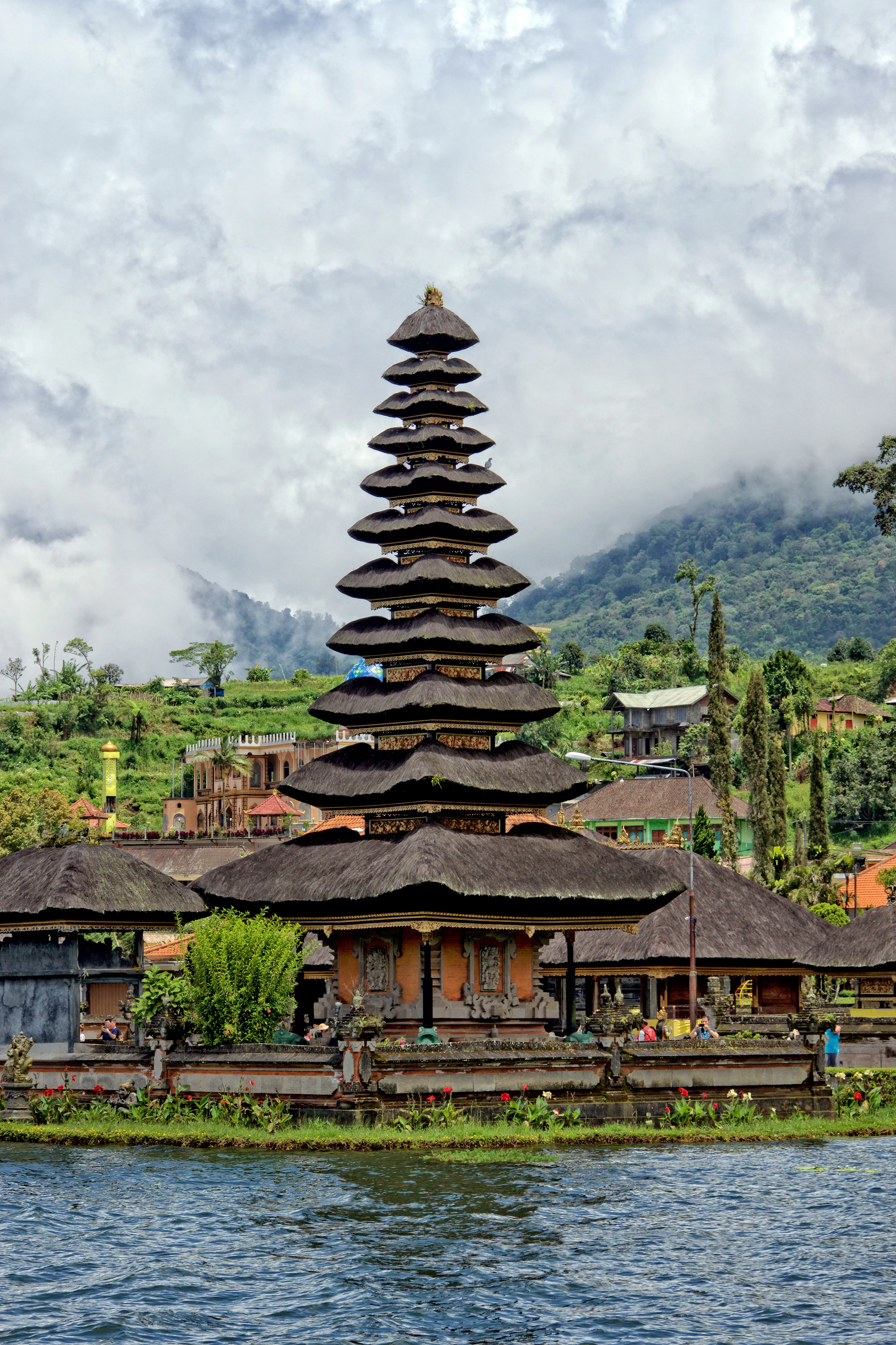 A multi-tiered thatched meru shrine on the water with mist behind
