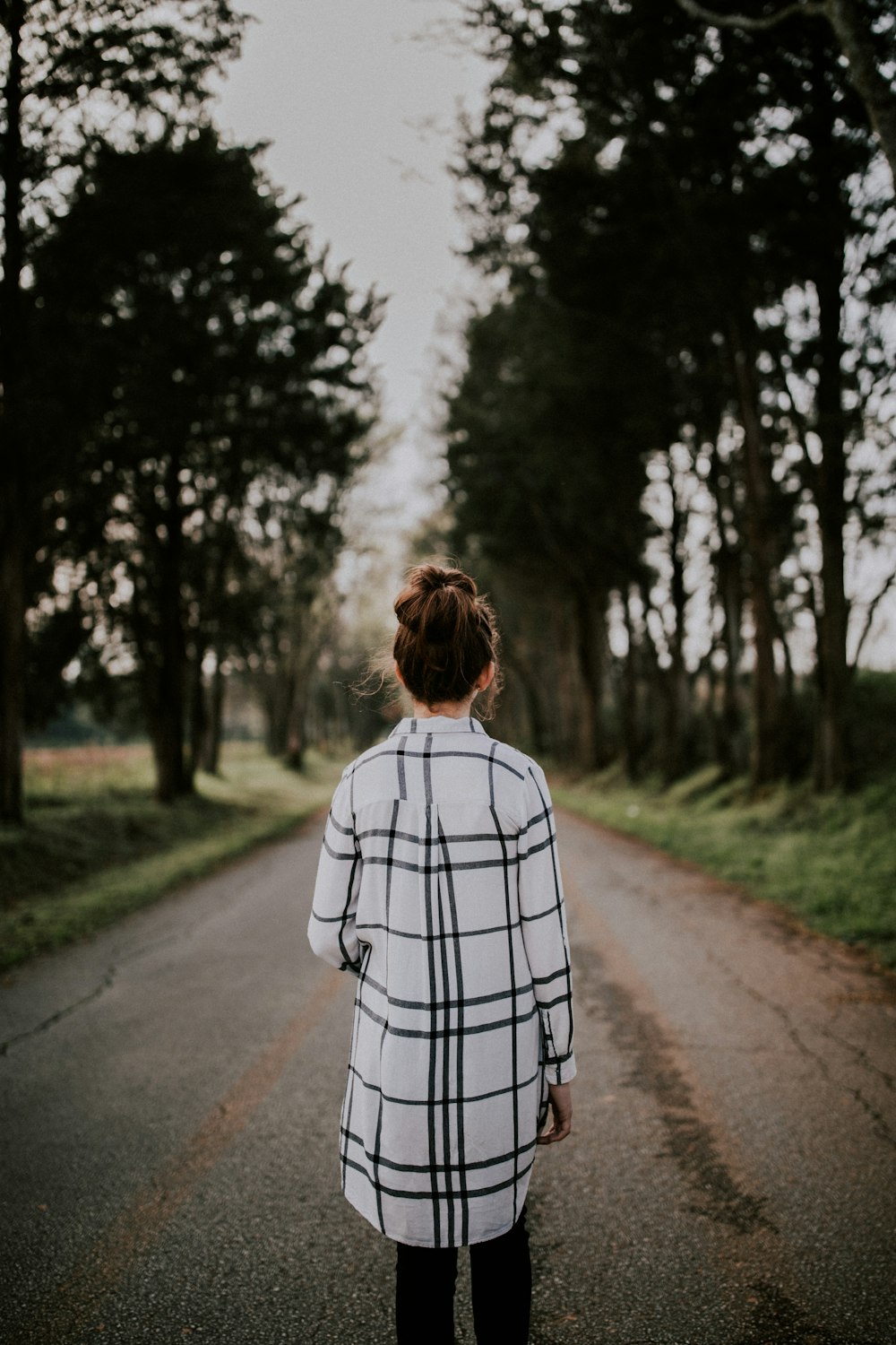 Fotografia con obiettivo tilt-shift di donna in piedi su una strada grigia circondata da alberi