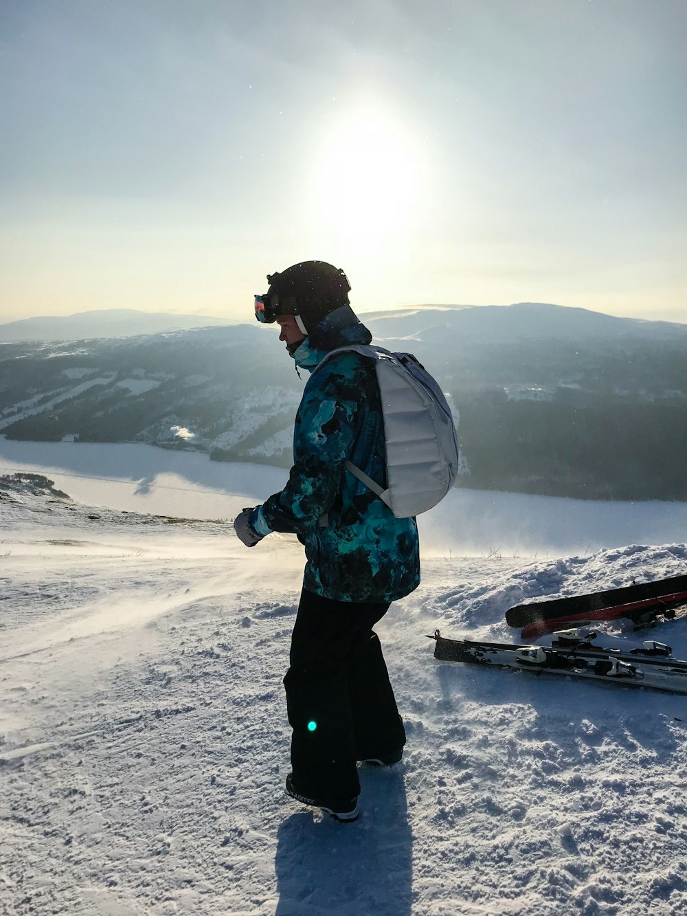 person with backpack standing on snow field looking down