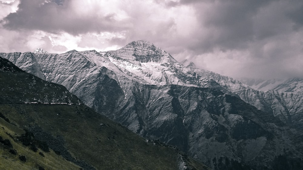 white snow cap mountain near green mountain under cloudy sky at daytime