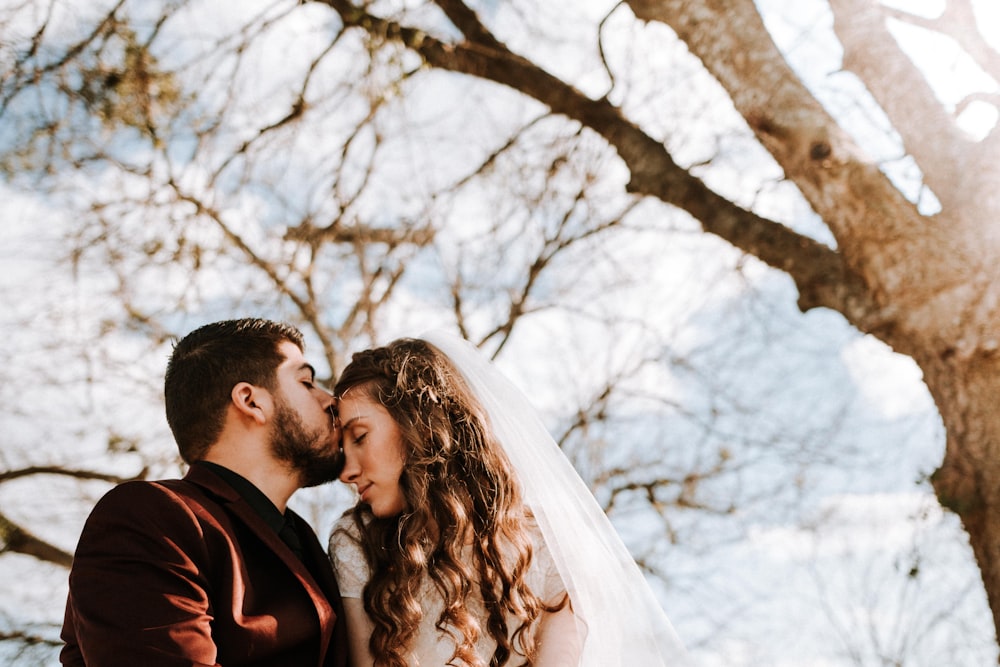 man kissing woman on forehead near bare tree during daytime