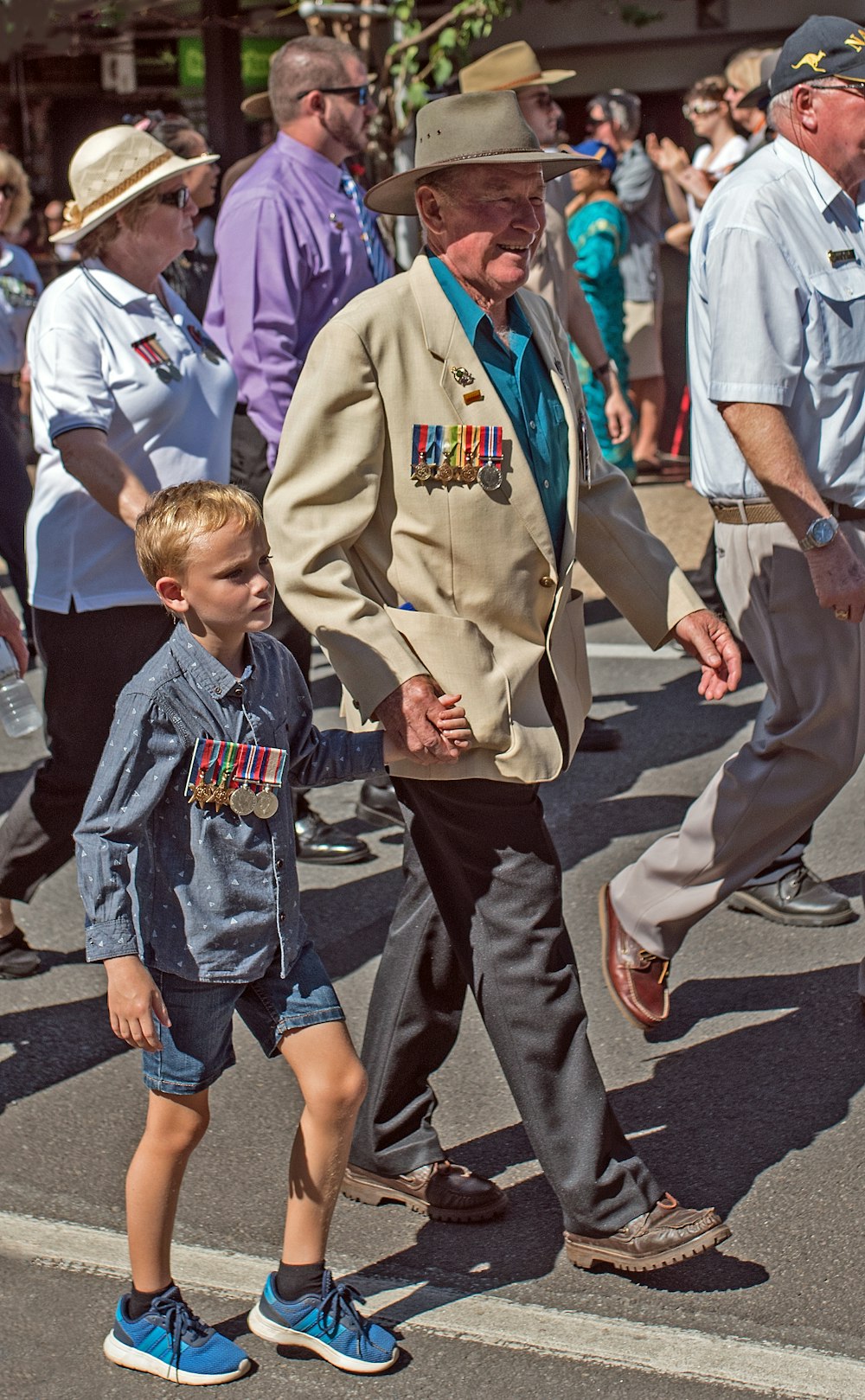 smiling man holding hand of boy while walking on road near people during daytime