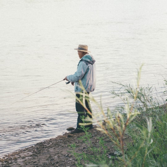 man fishing beside body of water during daytime photo in Saskatoon Canada