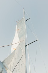 A single sail with ropes and mast extends upward against a clear sky. The sail shows visible seams and lines, and the top is angled slightly with some orange markers.