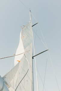 A single sail with ropes and mast extends upward against a clear sky. The sail shows visible seams and lines, and the top is angled slightly with some orange markers.