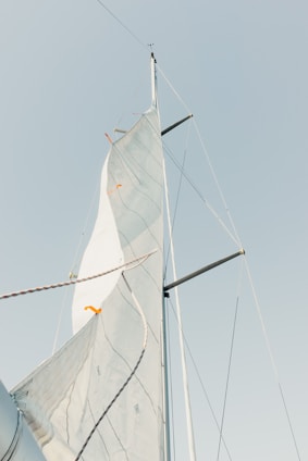 A single sail with ropes and mast extends upward against a clear sky. The sail shows visible seams and lines, and the top is angled slightly with some orange markers.