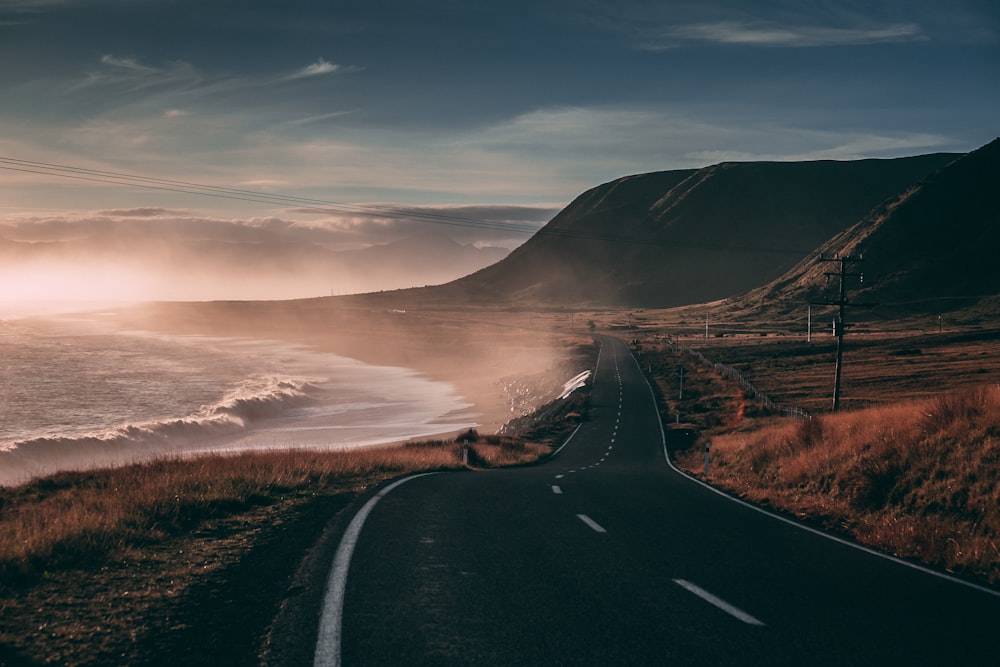 black road besides seashore and mountain at sunset