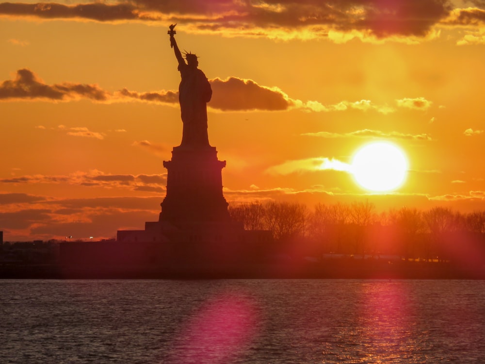 Silhouette der Freiheitsstatue unter orangefarbenem Sonnenuntergang