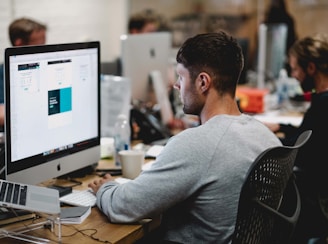 man in gray sweatshirt sitting on chair in front of iMac