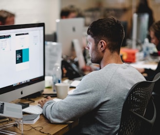 man in gray sweatshirt sitting on chair in front of iMac