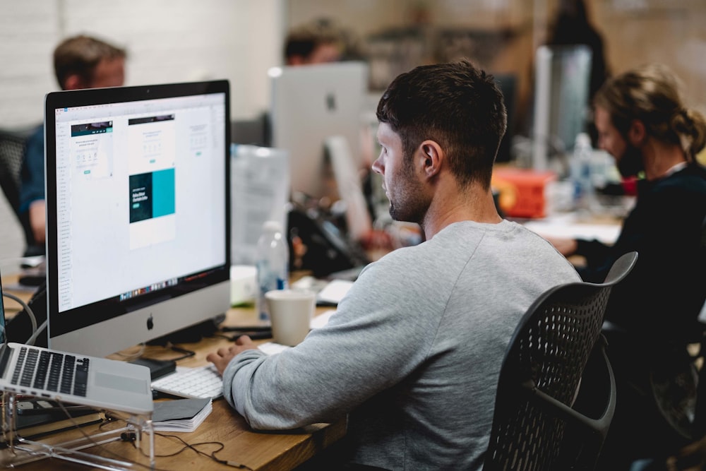 man in gray sweatshirt sitting on chair in front of iMac