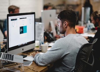 man in gray sweatshirt sitting on chair in front of iMac