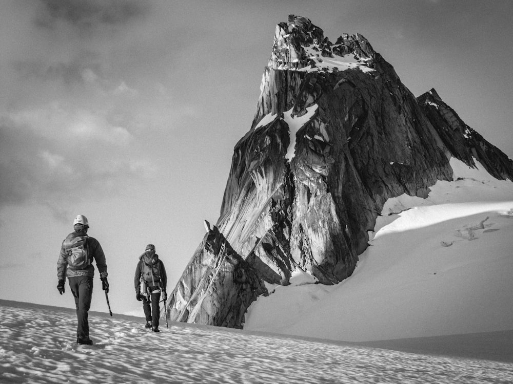 grayscale photo of two people walking on mountain valley