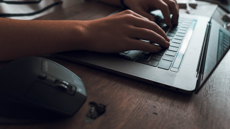 Hands typing on a wireless keyboard next to a stylish computer mouse.