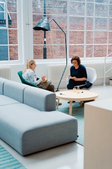 two woman sits on sofa chairs inside house