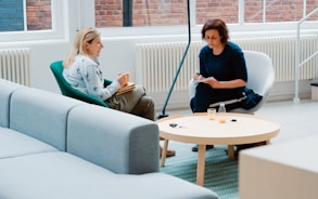 two woman sits on sofa chairs inside house