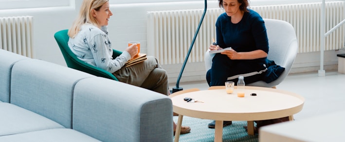 two woman sits on sofa chairs inside house