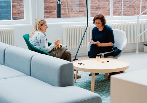 two woman sits on sofa chairs inside house