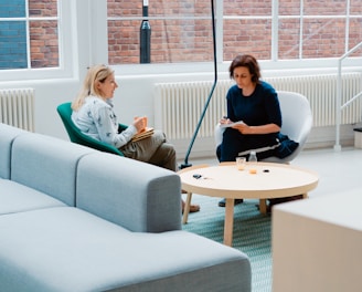 two woman sits on sofa chairs inside house