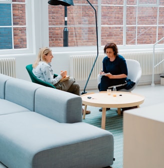 two woman sits on sofa chairs inside house