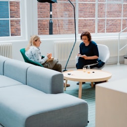 two woman sits on sofa chairs inside house