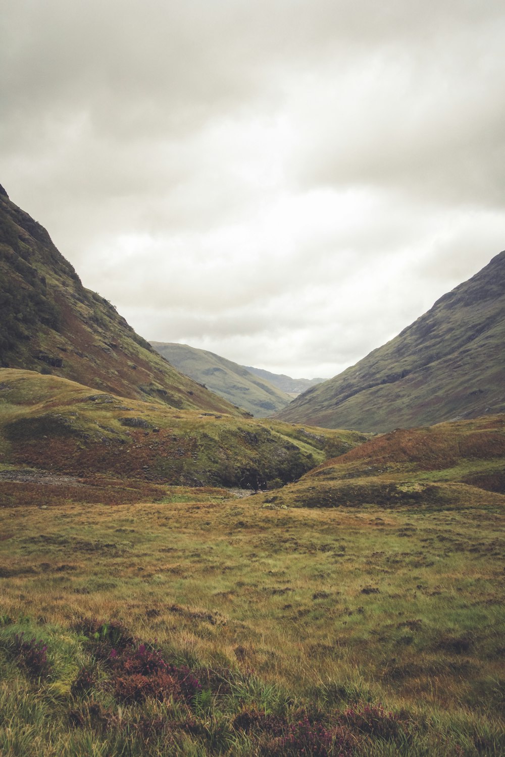 green grass field near mountain range during cloudy daytime