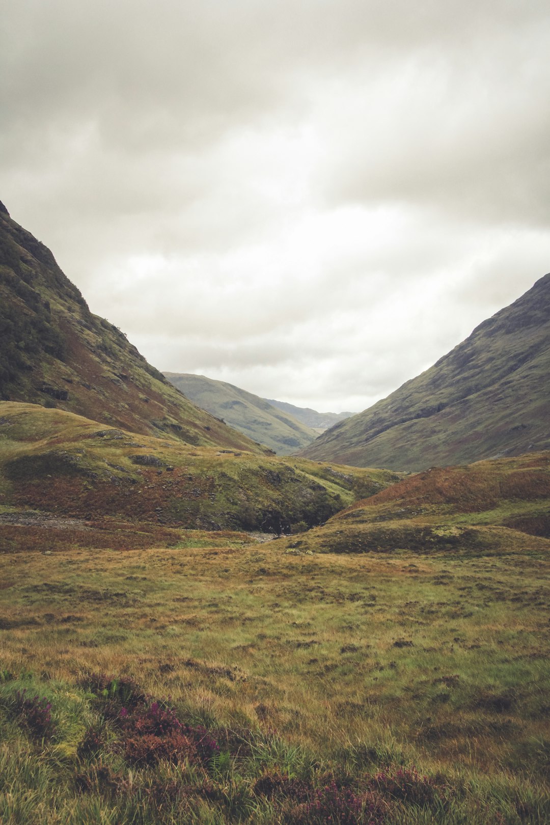 green grass field near mountain range during cloudy daytime