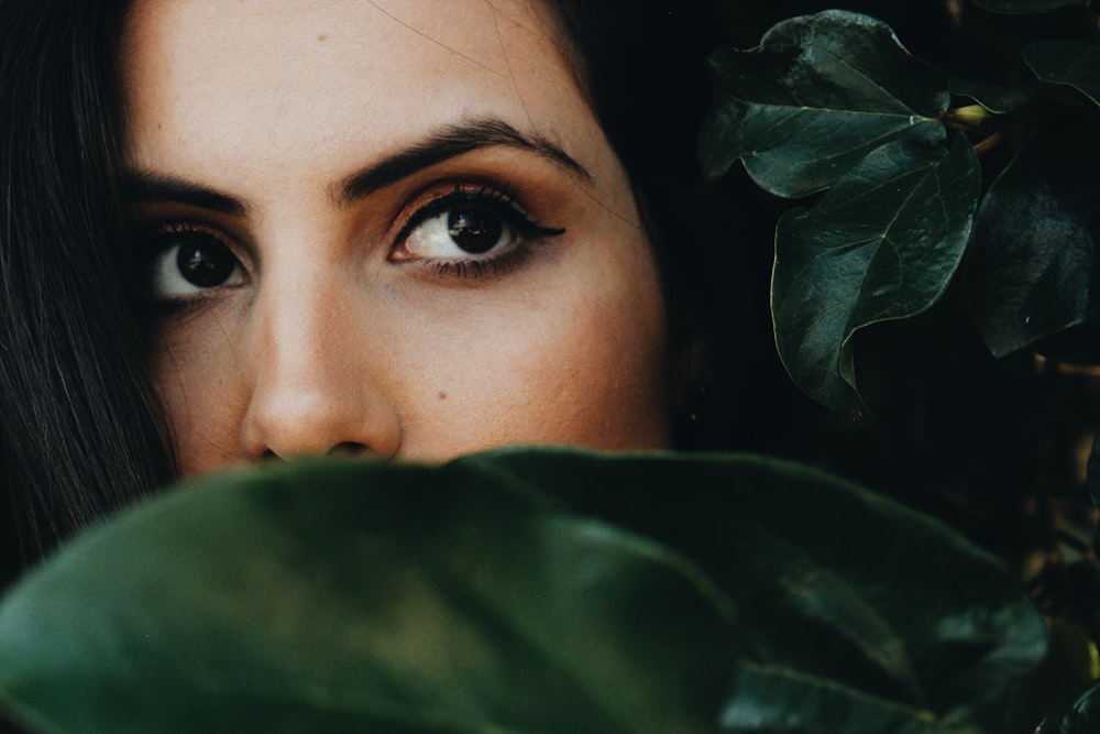 Frau mit halbem Gesicht in der Nähe von grünen Blättern