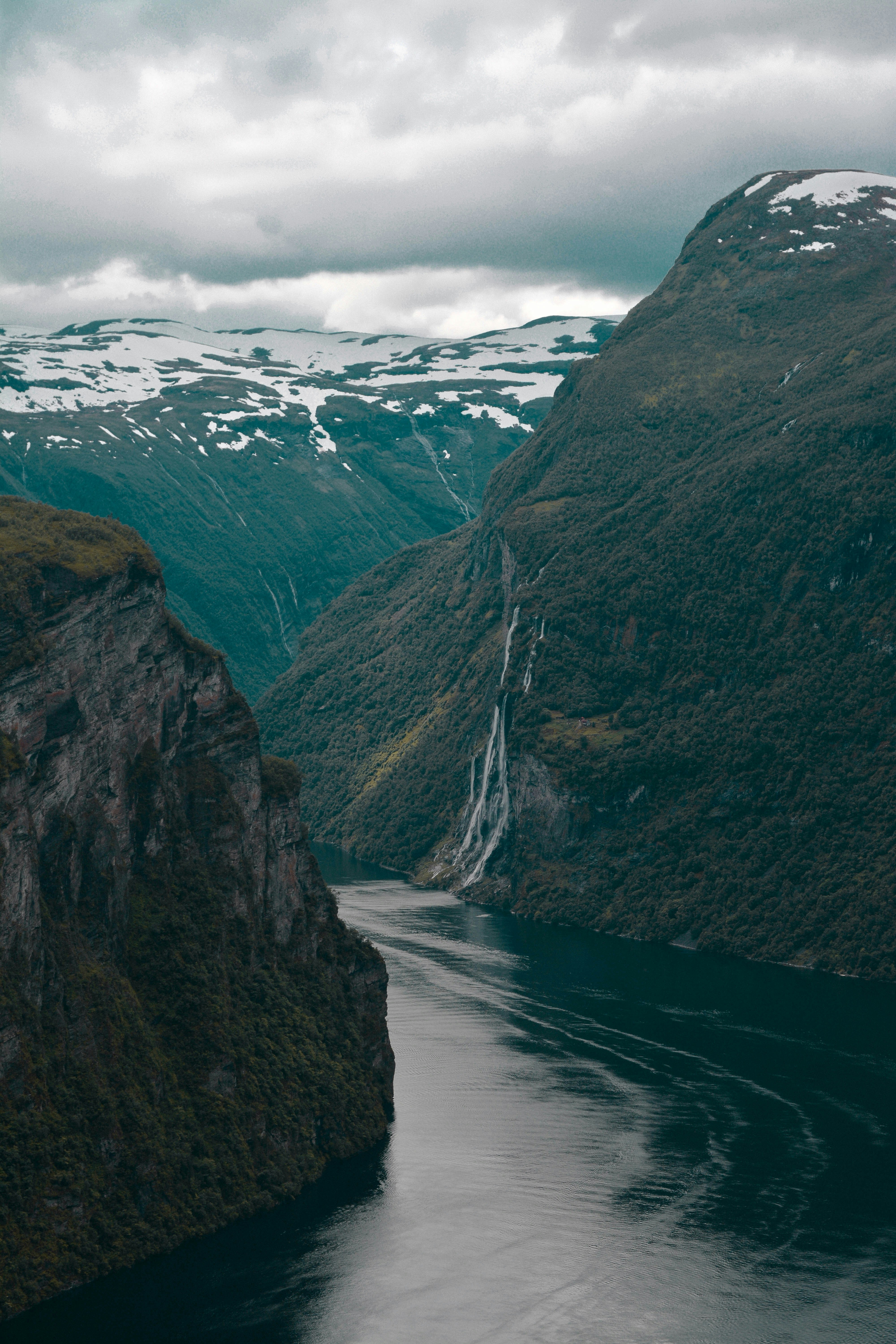Dramatic Patagonian fjord with turquoise glacial water, dark granite peaks, moody overcast sky
