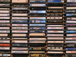 A collection of cassette tapes arranged neatly in stacks. Each tape displays the names of various music albums and artists, featuring diverse genres and time periods. The tapes are weathered and evoke a sense of nostalgia.