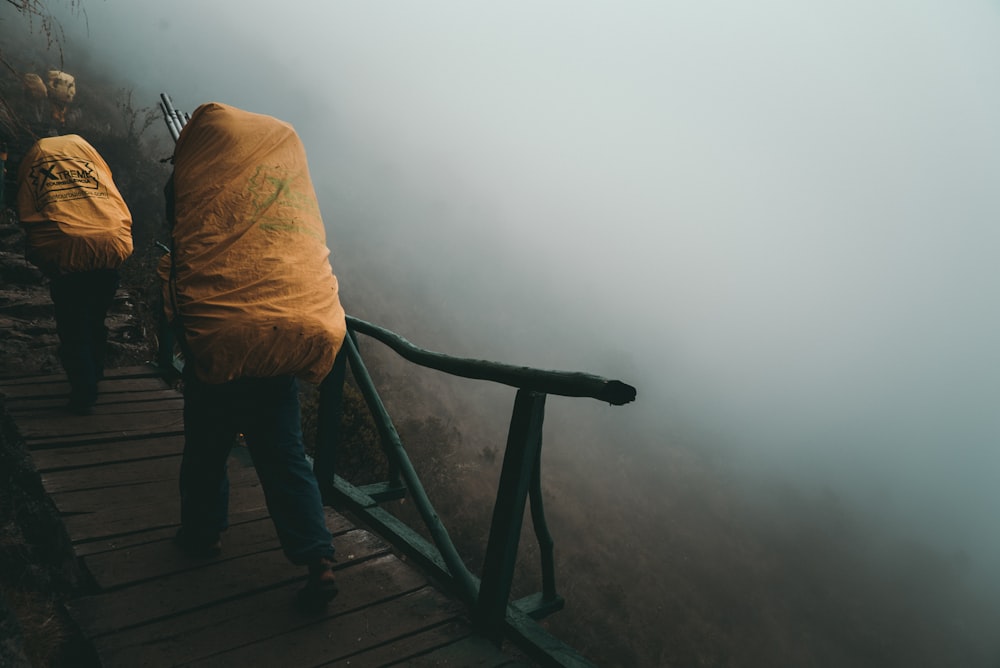 person in brown jacket and blue denim jeans standing on brown wooden stairs