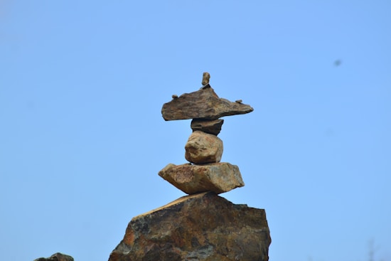 A balanced stack of rough, irregularly shaped stones atop a larger rock against a clear blue sky.